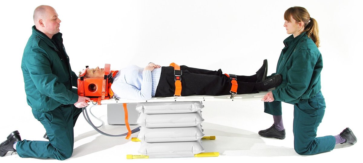 Patient on a long board with head blocks and body straps, two paramedics at head and feet