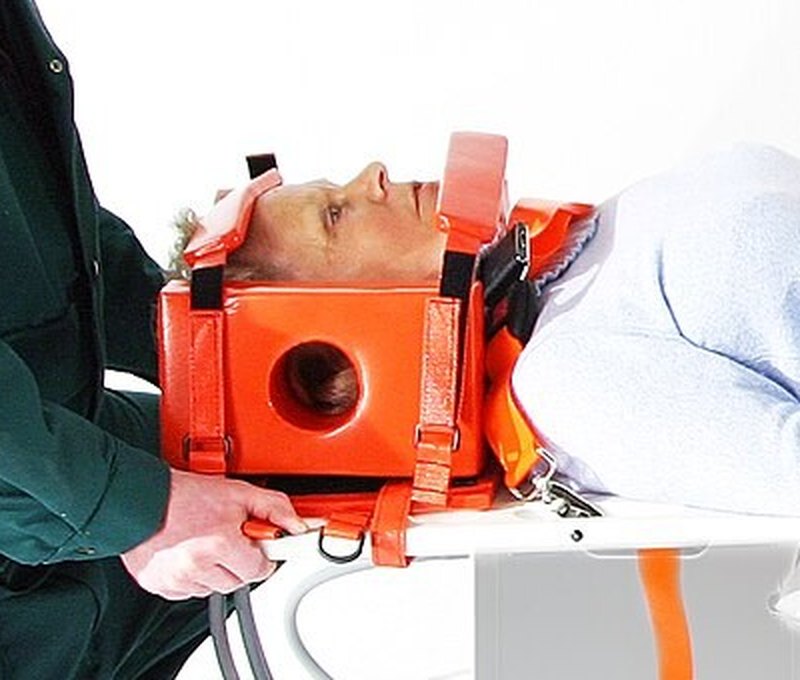 Head immobiliser: orange lateral head blocks with forehead and chin straps on a board, ear opening visible